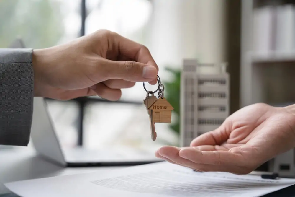 A mão de um homem entregando a chave de uma casa para outro homem