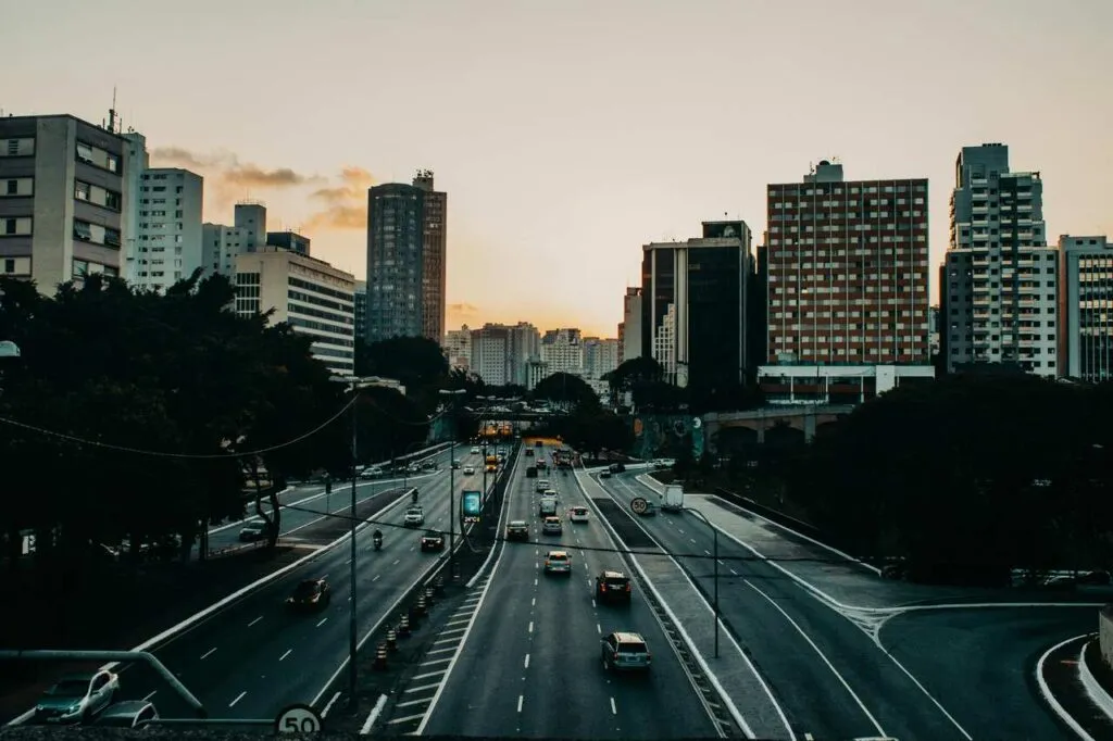 Avenida movimentada em São Paulo ao entardecer, cercada por prédios altos.