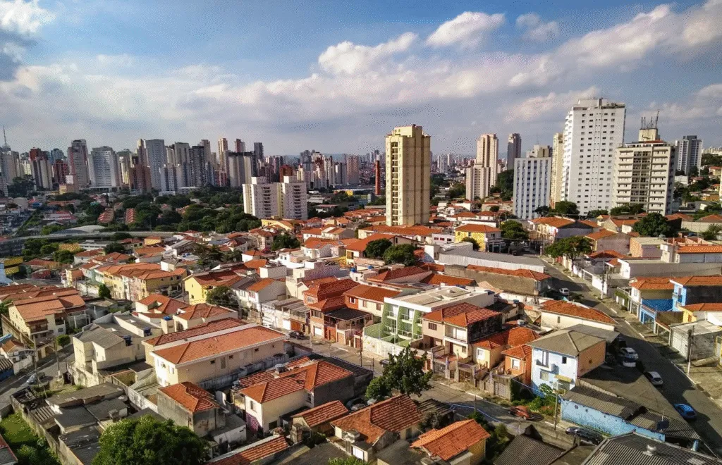 Vista aérea da Vila Mariana com casas de telhado vermelho e prédios altos ao fundo em um dia ensolarado em São Paulo.